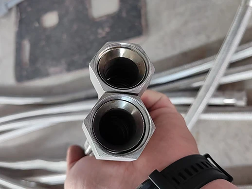 A worker holding two braided metal hoses with internal threaded joints